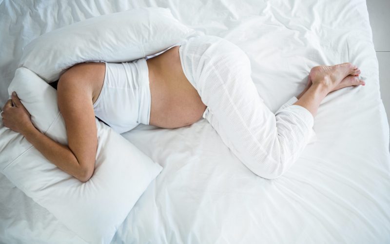 High angle view of pregnant woman with head under pillow on bed